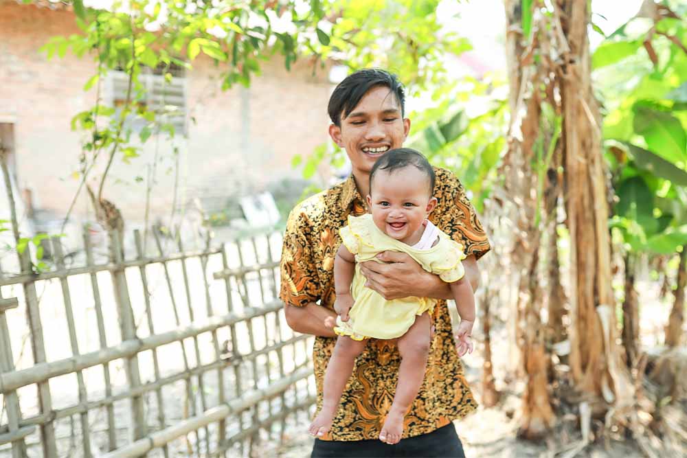 Umar smiling and holding Putri after her cleft surgery