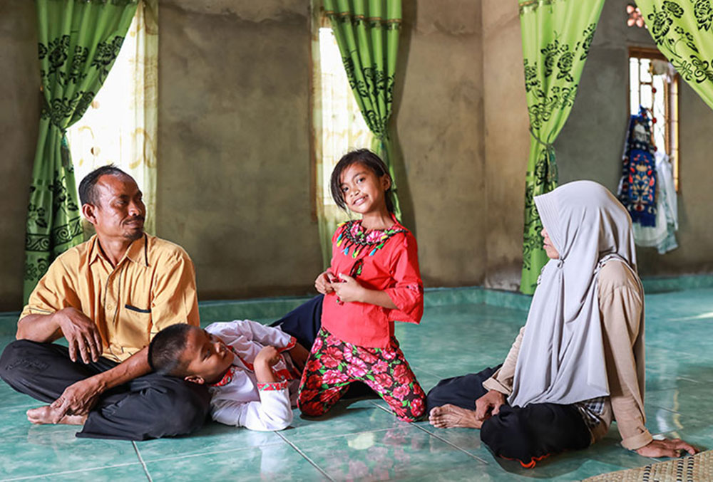 Aira smiling and sitting with her family at the mosque after cleft surgery