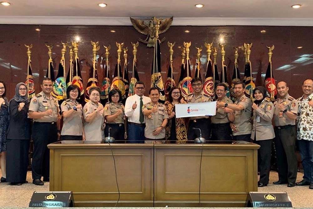 Petugas kepolisian Indonesia tersenyum bersama staf Smile Train, memegang tanda Smile Train dan mengacungkan jempol