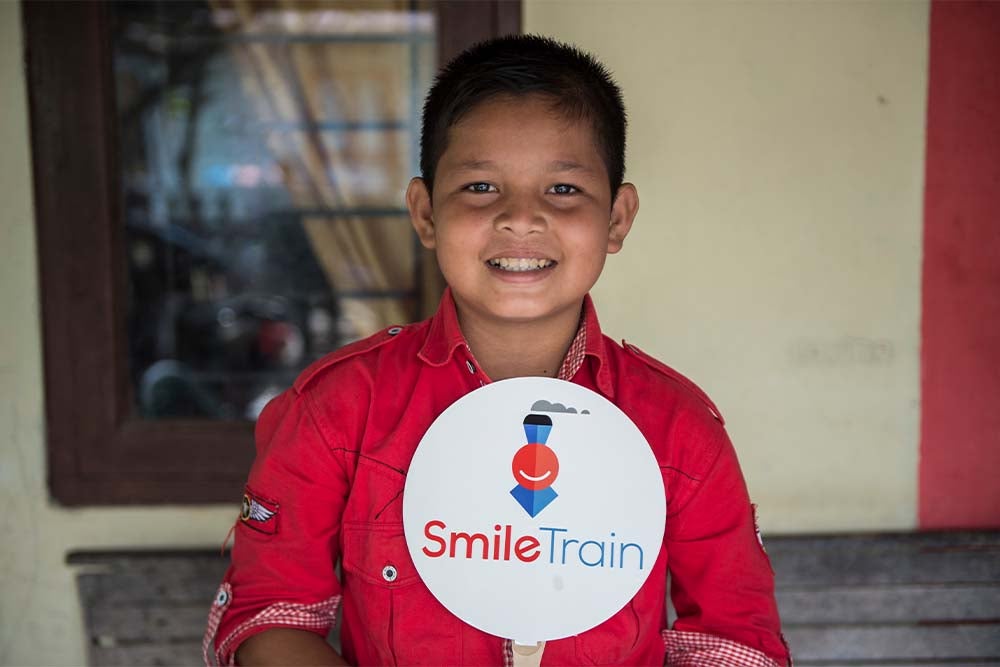 Deri tersenyum usai operasi sumbing dan memegang tanda Smile Train