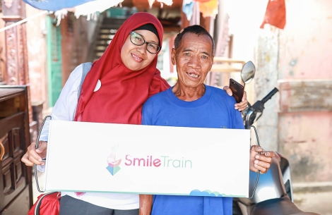 Endang smiling and holding a Smile Train banner with an older patient