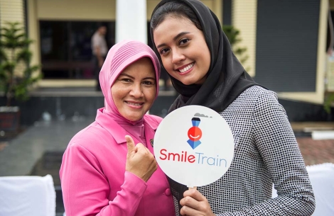 Pendukung Smile Train tersenyum dan memegang tanda Smile Train dalam perjalanan Perjalanan Senyum