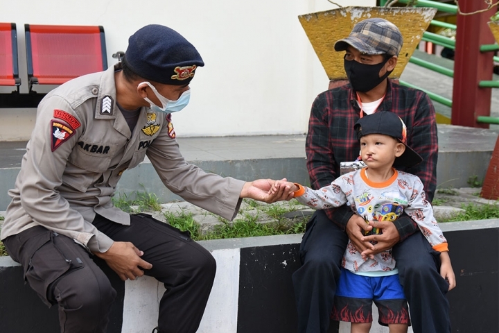 Petugas polisi Indonesia memegang tangan seorang anak penderita sumbing dan ayah mereka