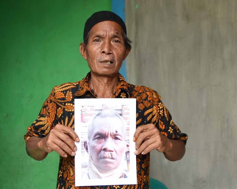 Older Smile Train patient smiling and holding a photo of himself before cleft surgery